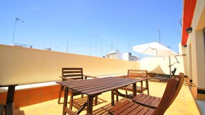 A rooftop terrace with a wooden table and chairs, a white umbrella, and a view of the city skyline. - Living Sevilla Centro Maestranza (Seville)