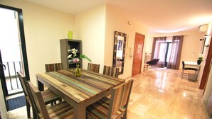 A dining area with a wooden table, chairs, and a vase with flowers. There is a mirror on the wall and a door leading to another room. - Living Sevilla Centro Maestranza (Seville)