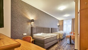 Camera d'albergo con un letto, una scrivania, una sedia, un tavolino e una finestra con tende.