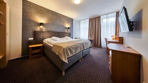 Una camera d'albergo con un letto, comodini, una scrivania, una sedia, una televisione e una finestra con tende.