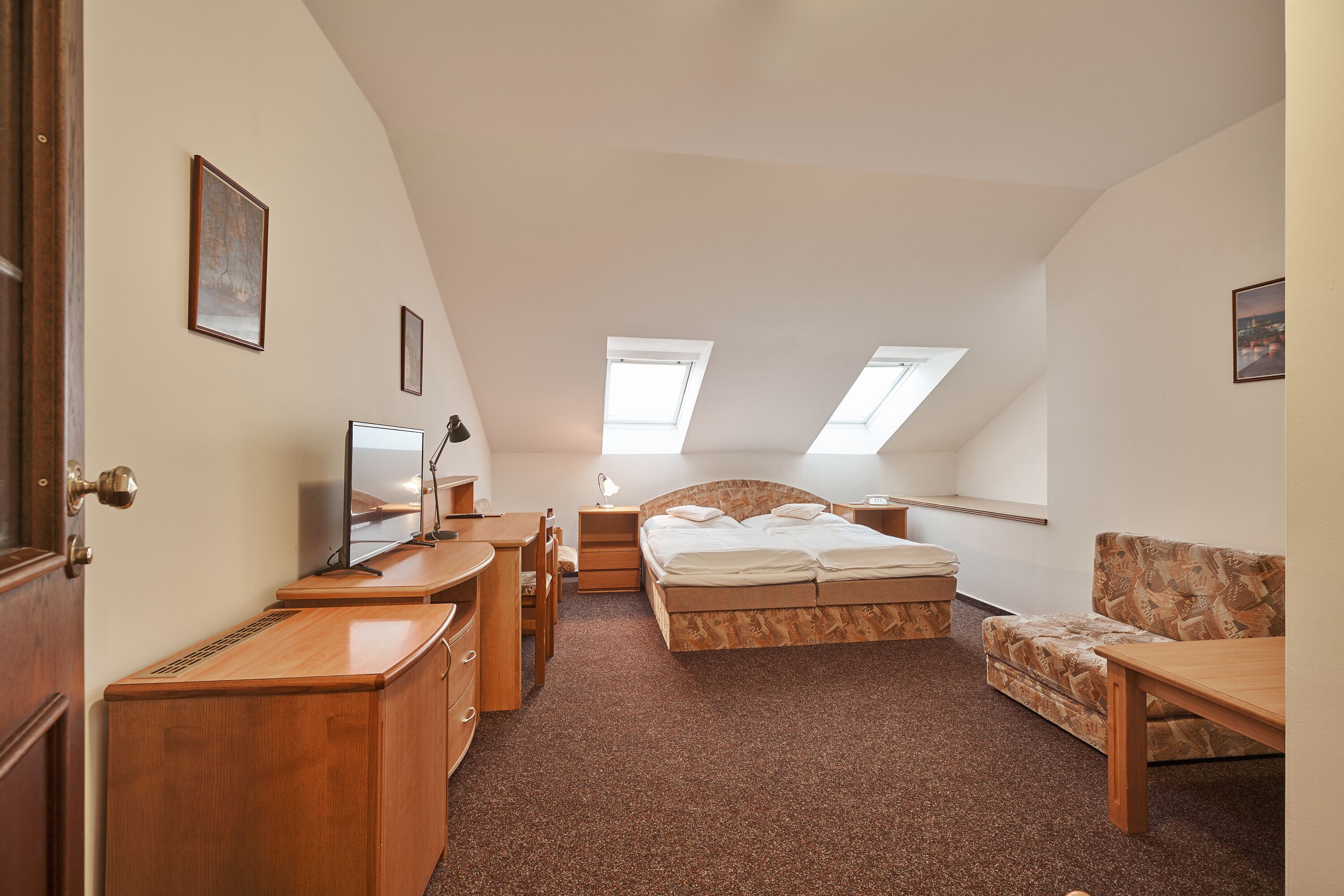 A bedroom with a bed, desk, chair, and a small table. There are skylights on the ceiling.