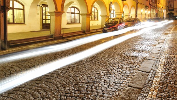 Scena notturna di una strada con un edificio caratterizzato da numerose finestre e porte ad arco.