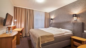Ein Hotelzimmer mit Bett, Schreibtisch mit Stuhl, Fernseher und Wandlampe.