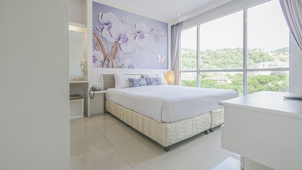 A modern bedroom with a large bed, a bedside table, a nightstand, and a view of greenery through the window.