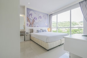 A modern bedroom with a large bed, a bedside table, a nightstand, and a view of greenery through the window. - Sino Maison Hotel (Patong)