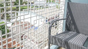 A balcony with a wicker chair, a white metal railing, and a view of buildings and greenery.