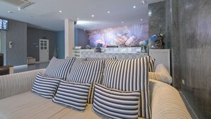 A modern hotel lobby with a reception desk, a sofa with striped cushions, and a mural with tropical elements.