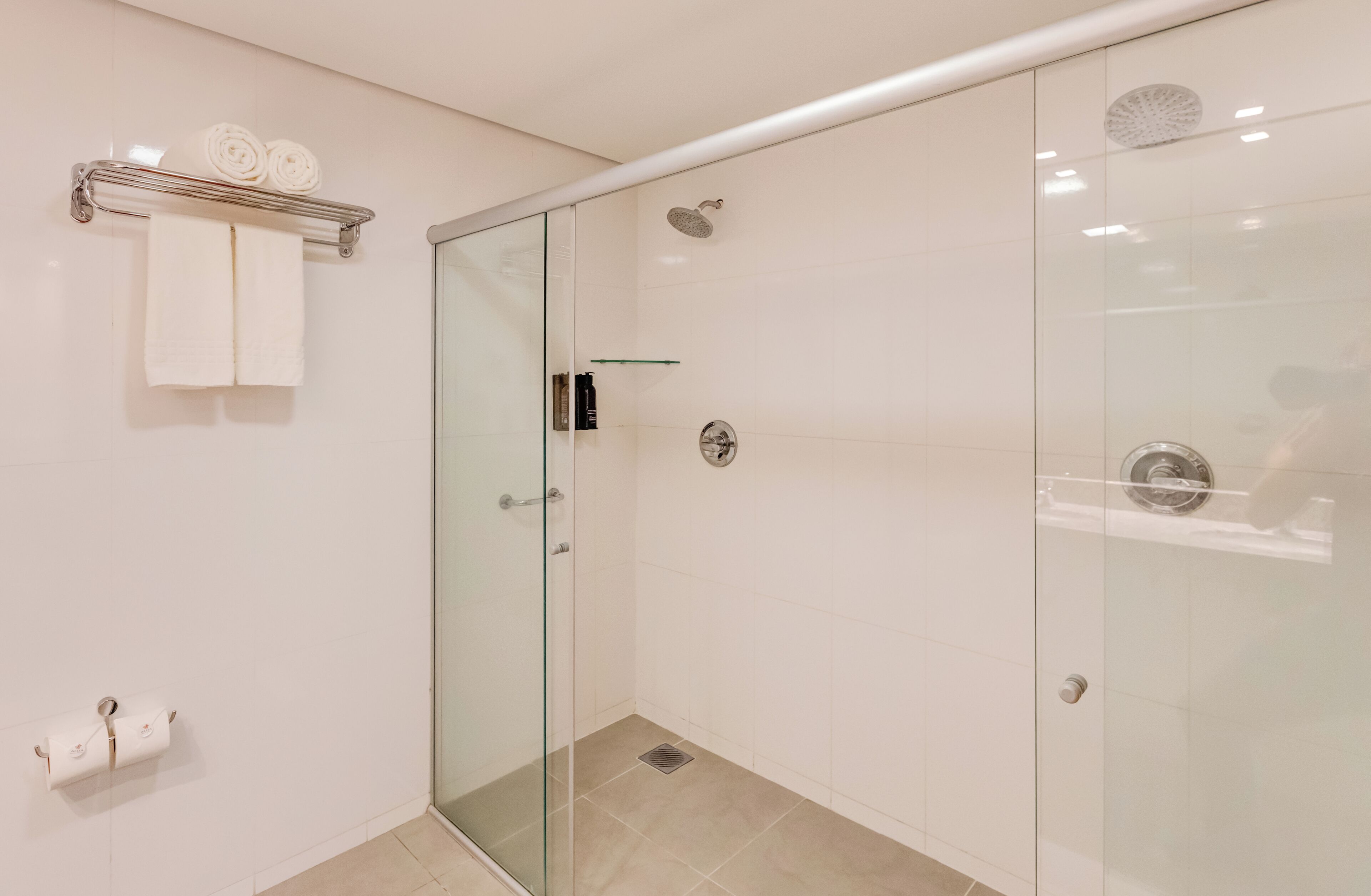 Un baño moderno con cabina de ducha de vidrio, un perchero con toallas dobladas y un dispensador de papel higiénico.