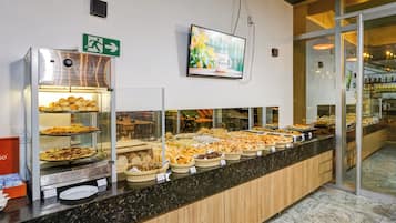Uma área de buffet com diversos produtos de panificação e uma televisão fixada na parede.