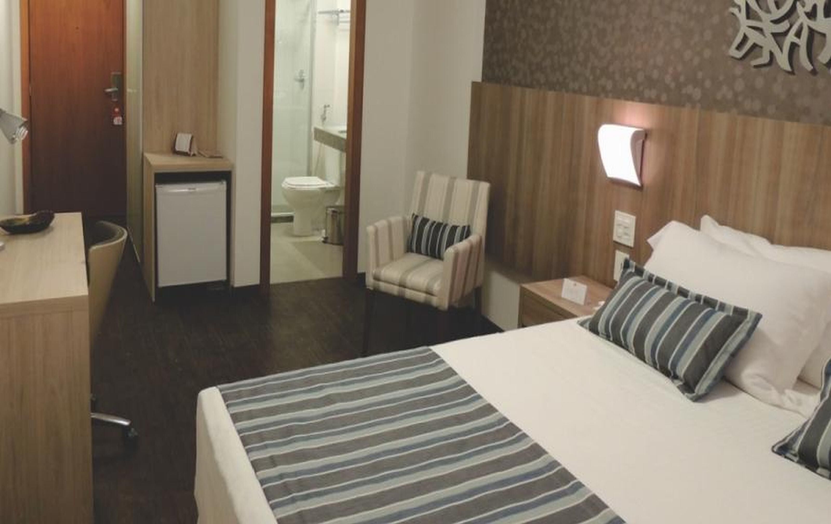 Une chambre d’hôtel avec un lit, un bureau, une chaise et une petite salle de bain.