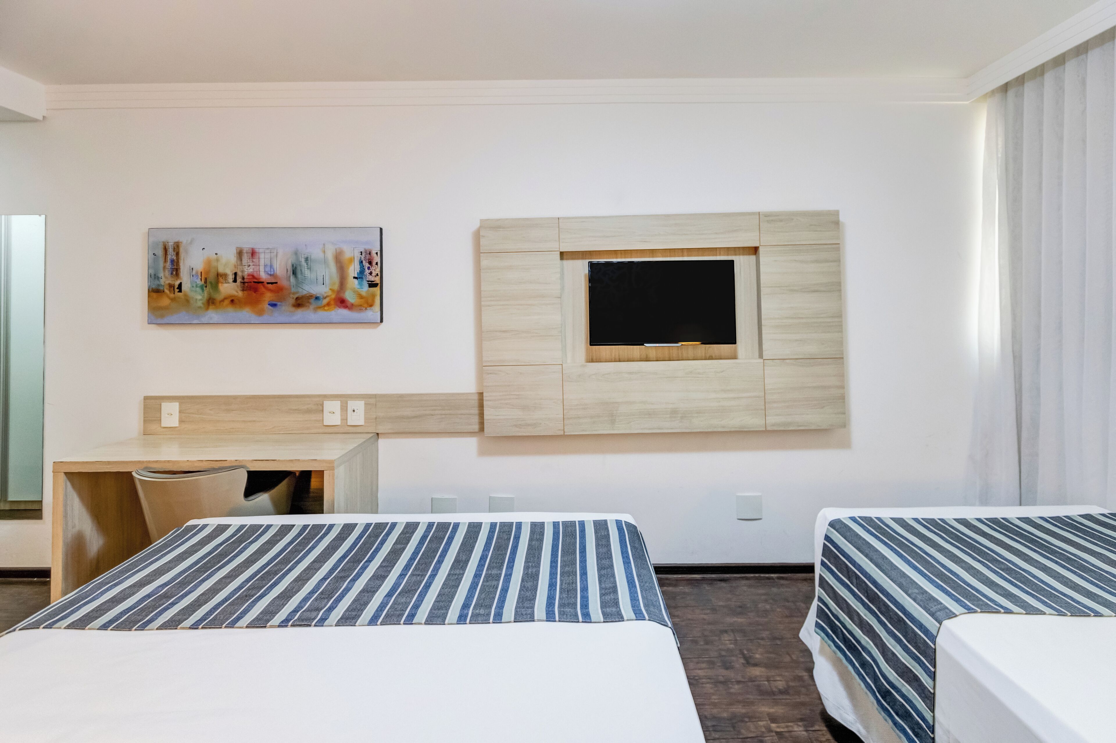 A hotel room with two beds, a desk, a TV, and a painting on the wall.