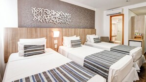 Hotelkamer met drie bedden, een decoratief kunstwerk, een nachtkastje en een klein bureau met een lamp.