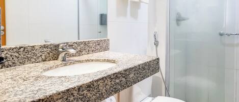 Une salle de bain moderne avec un comptoir en granit, des toilettes blanches et une cabine de douche en verre.