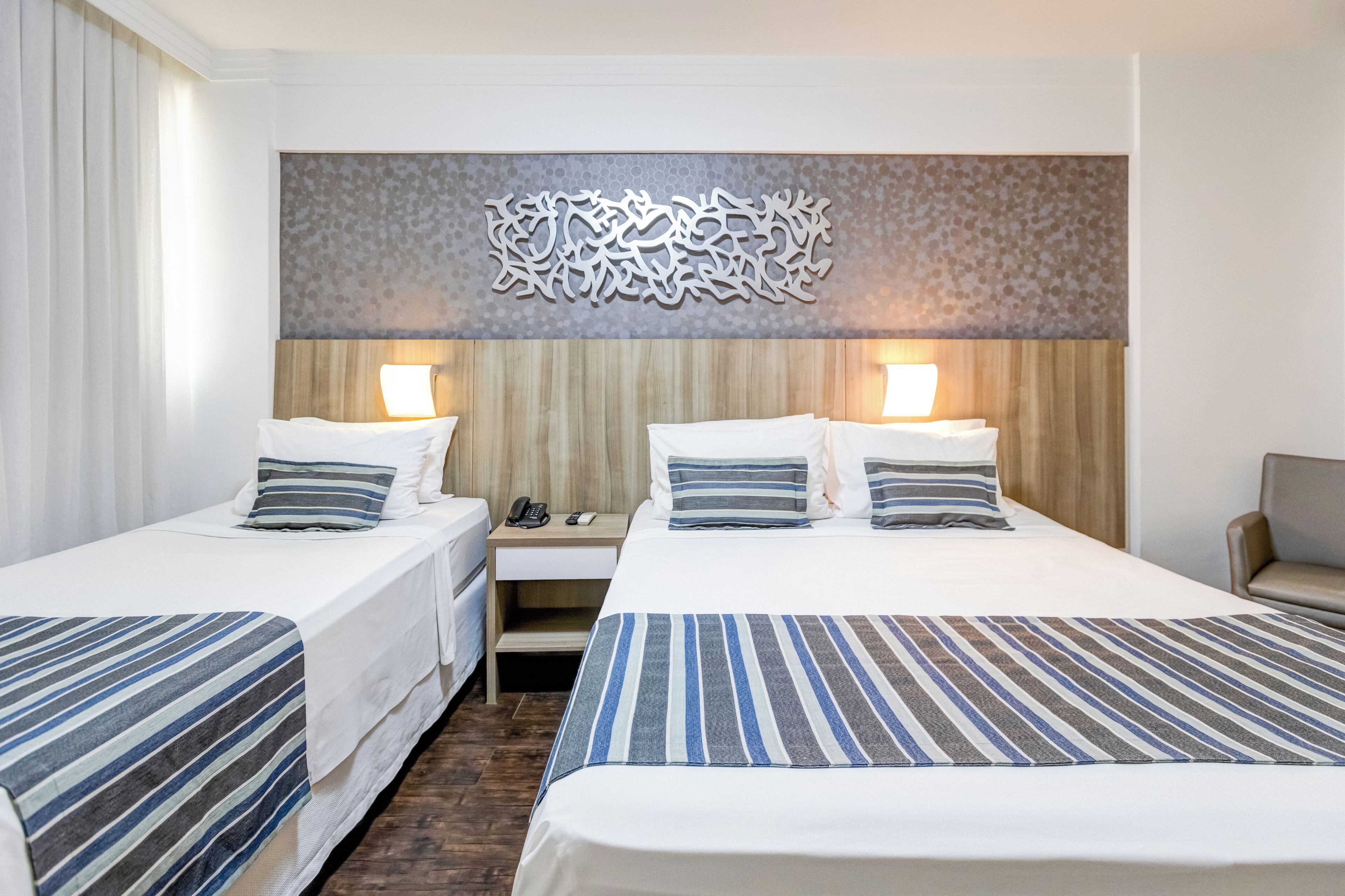 A hotel room with two beds, each with a striped bedspread, a wooden headboard, and a decorative wall piece above the beds.