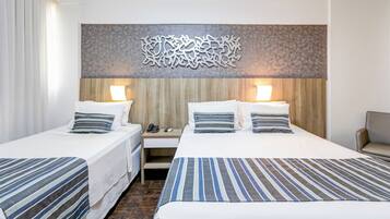 A hotel room with two beds, each with a striped bedspread, a wooden headboard, and a decorative wall piece above the beds.