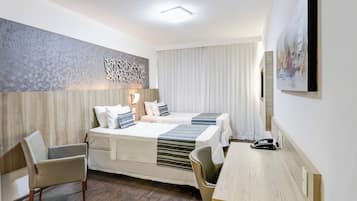Habitación de hotel con dos camas, un escritorio, una silla, un teléfono y un cuadro en la pared.