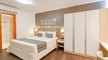 Quarto de hotel com cama, mesa de cabeceira, luminária, guarda-roupa e um objeto decorativo na parede.