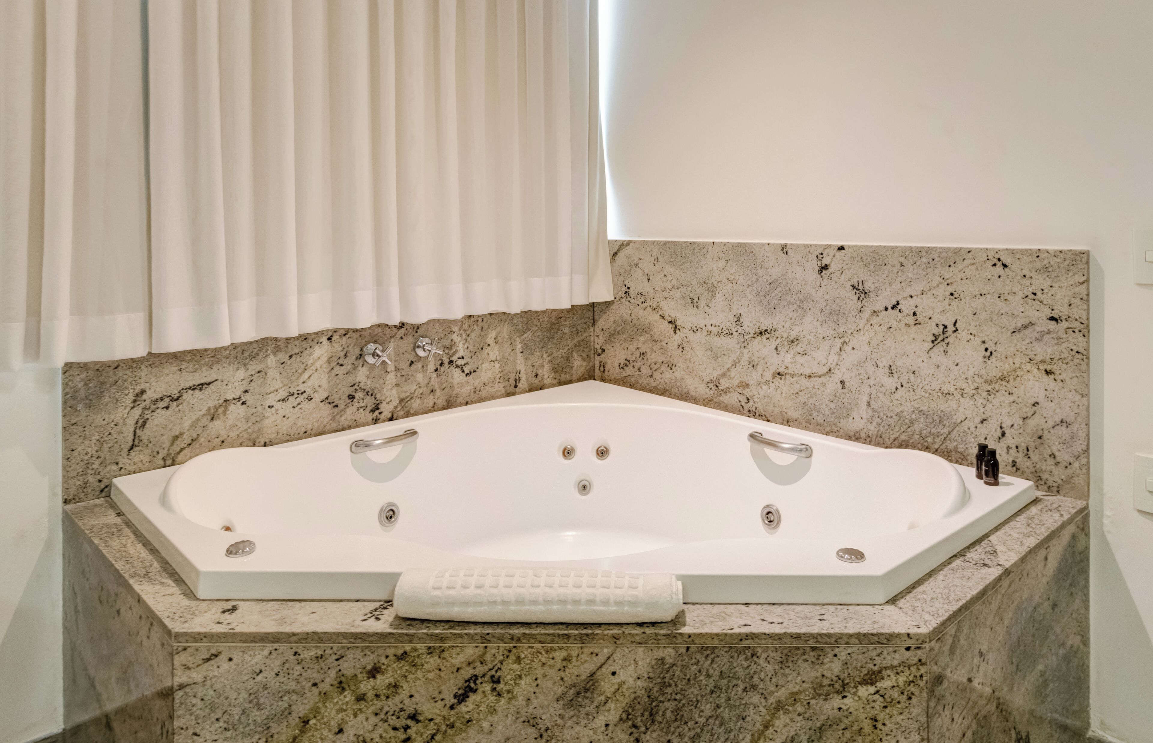 Un baño con bañera independiente, encimeras de mármol y una ventana con cortinas.
