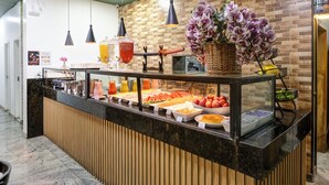 Een ontbijtbuffet met diverse soorten fruit en drankjes, een rieten mand met bloemen en een achtergrond van een bakstenen muur.
