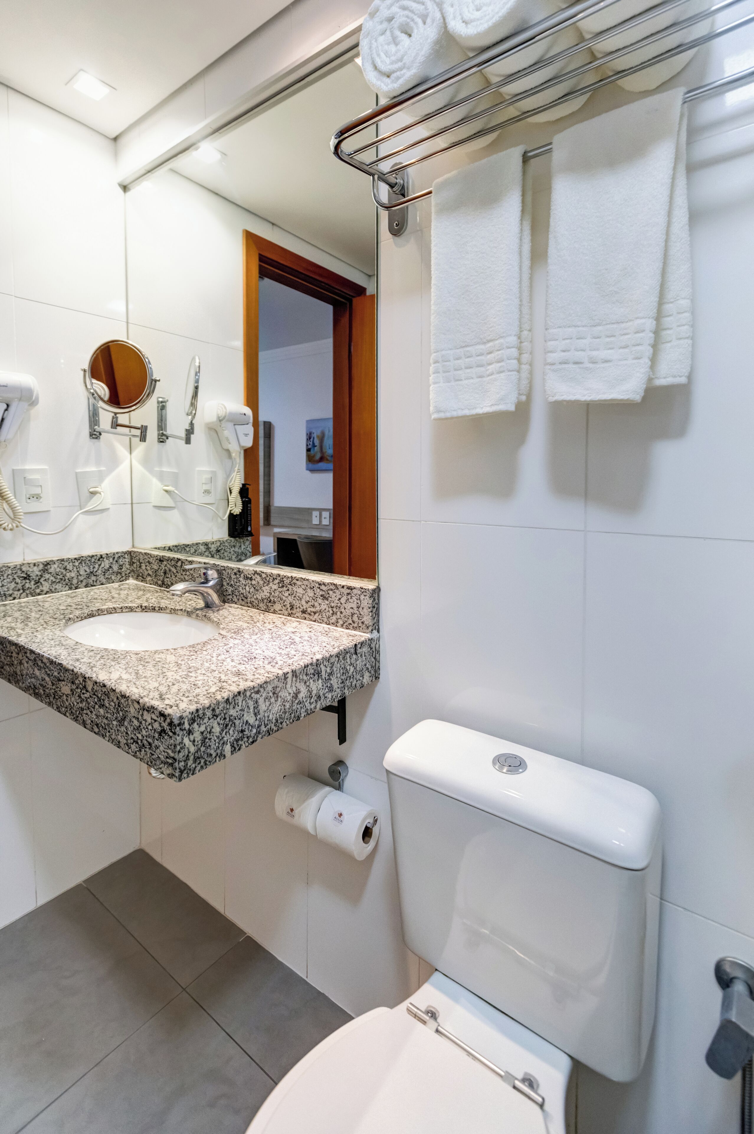 Casa de banho com lavatório de granito, sanita e porta-toalhas com toalhas.