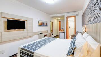 Una habitación de hotel con cama, televisor de pantalla plana en la pared, escritorio con silla y una kitchenette pequeña.