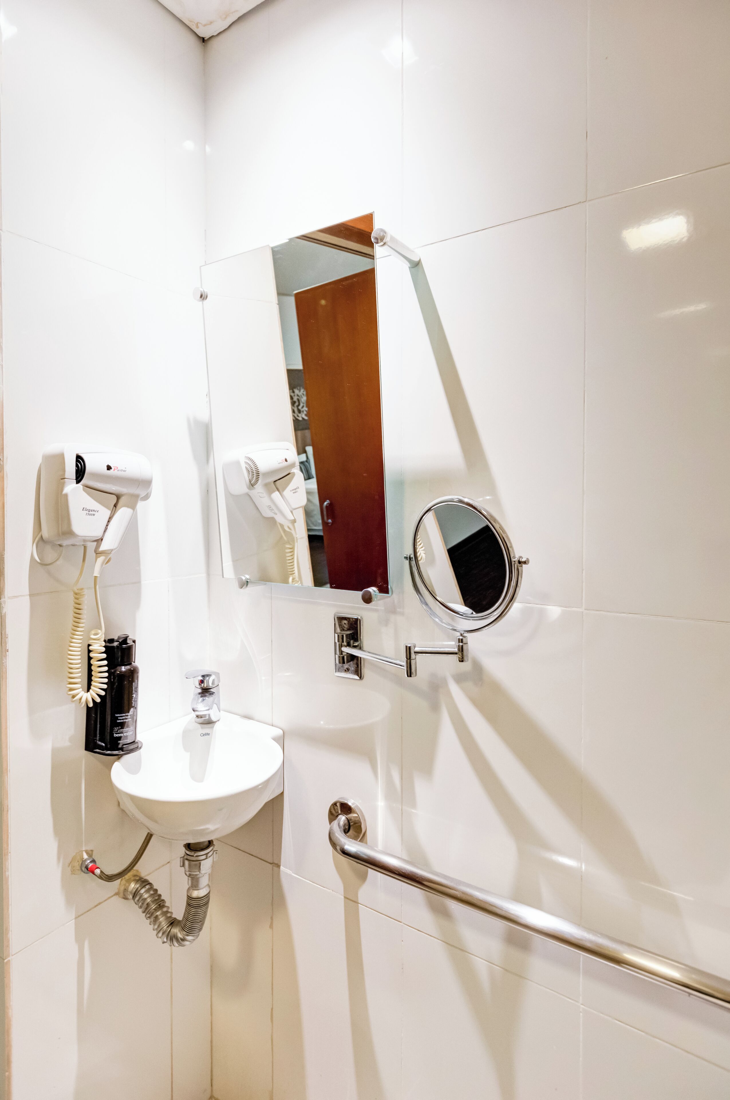 A bathroom with a white sink, a handheld hair dryer, a mirror, and a grab bar.