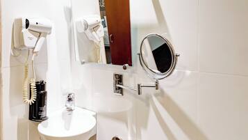 A bathroom with a white sink, a handheld hair dryer, a mirror, and a grab bar.