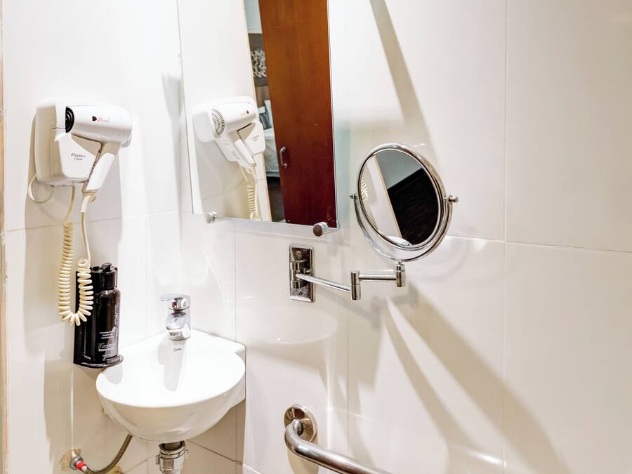 A bathroom with a white sink, a handheld hair dryer, a mirror, and a grab bar.