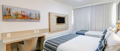 Habitación de hotel con cama, escritorio con silla, televisión montada en la pared y ventana con persianas.