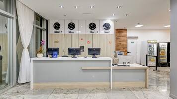 A reception desk with multiple monitors, a clock above it, and a vending machine to the right.