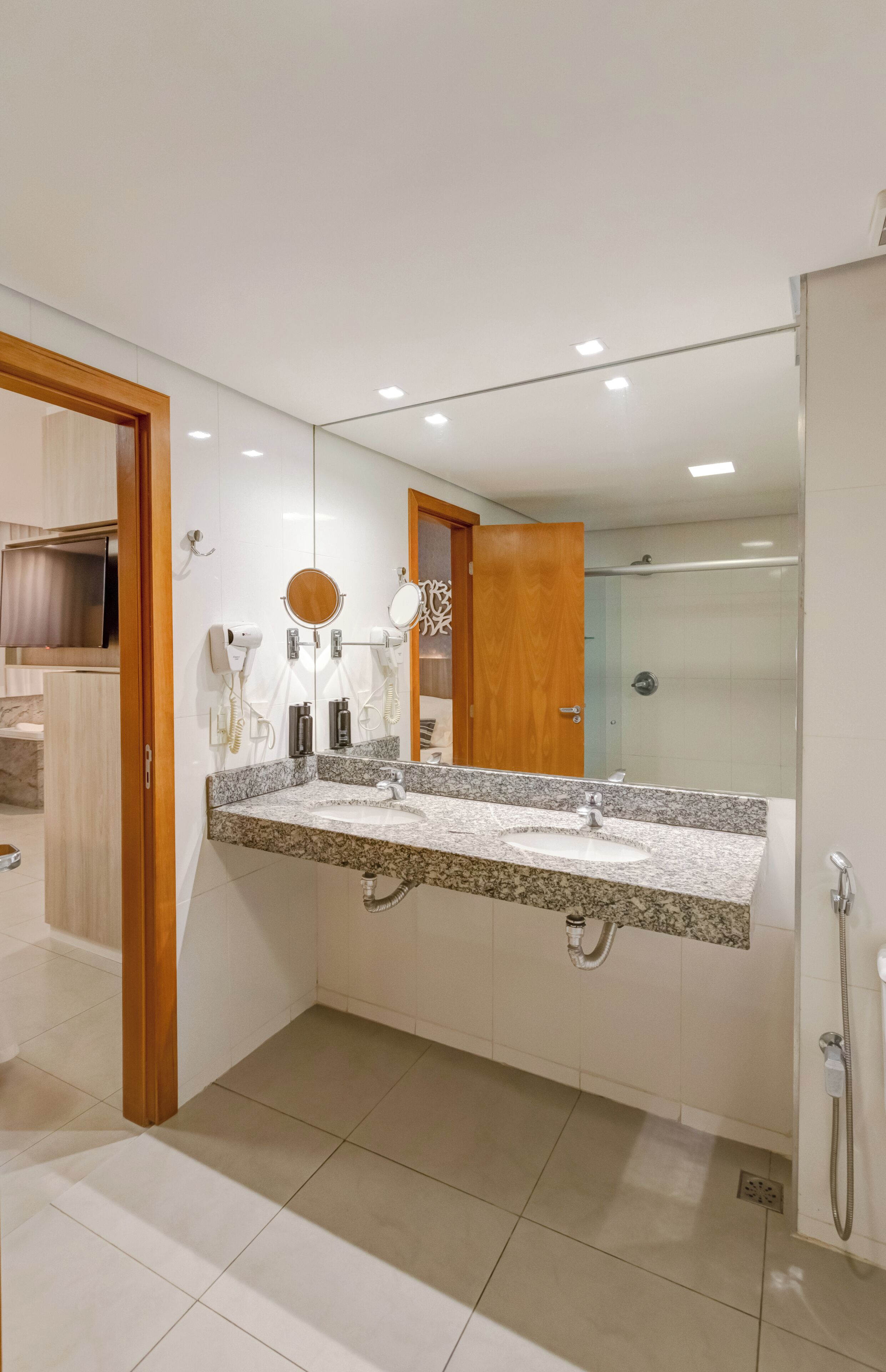 A modern bathroom with a granite countertop, a large mirror, a handheld showerhead, and a vanity with a sink.