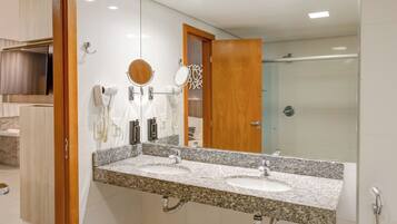 A modern bathroom with a granite countertop, a large mirror, a handheld showerhead, and a vanity with a sink.