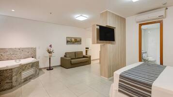A modern hotel room with a marble bathroom, a sofa, a flat-screen TV, and a bed with a striped bedspread.