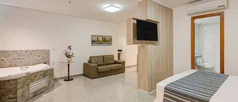 Una habitación de hotel moderna con baño de mármol, sofá, televisor de pantalla plana y cama con colcha a rayas.