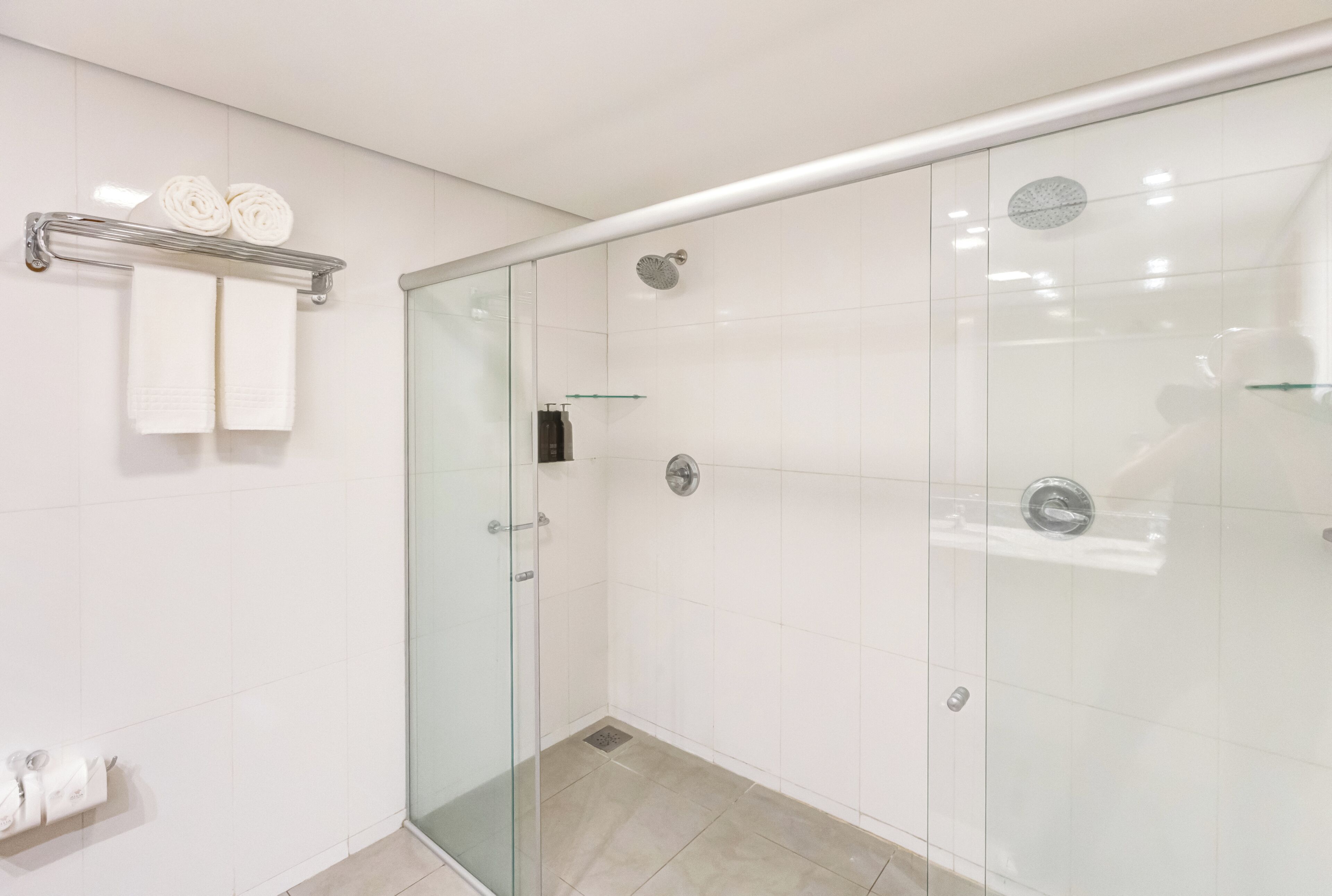 Ein modernes Badezimmer mit einer Duschkabine aus Glas, weißen Fliesen und einem Handtuchhalter mit gefalteten Handtüchern.
