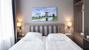 A hotel room with a bed, two bedside lamps, a wall-mounted phone, and a painting of a windmill. - Hotel Fine Harmony (Amsterdam)