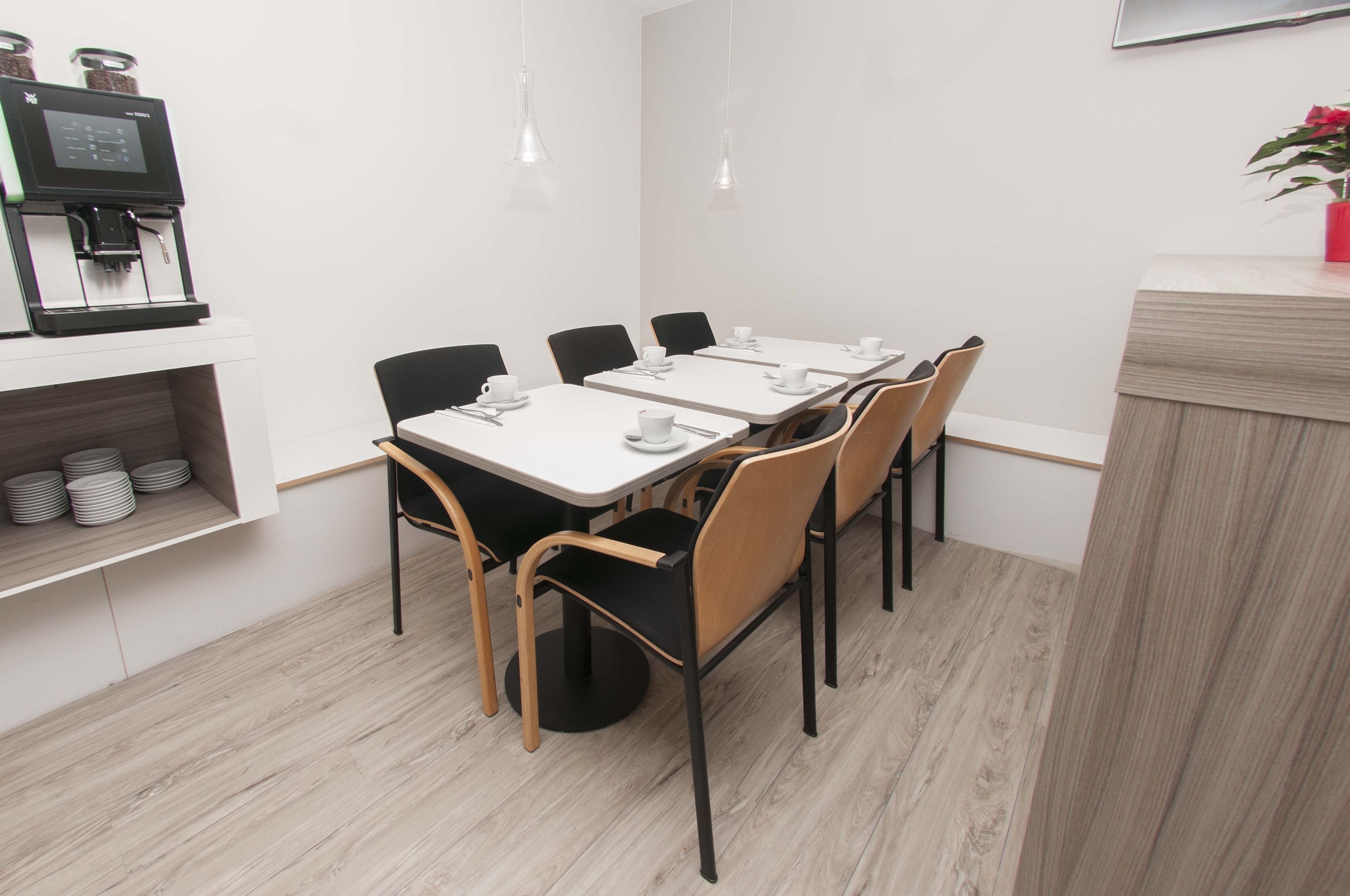 Un espace repas moderne avec une longue table, des chaises noires et en bois, de l’assiette blanche et une machine à café.