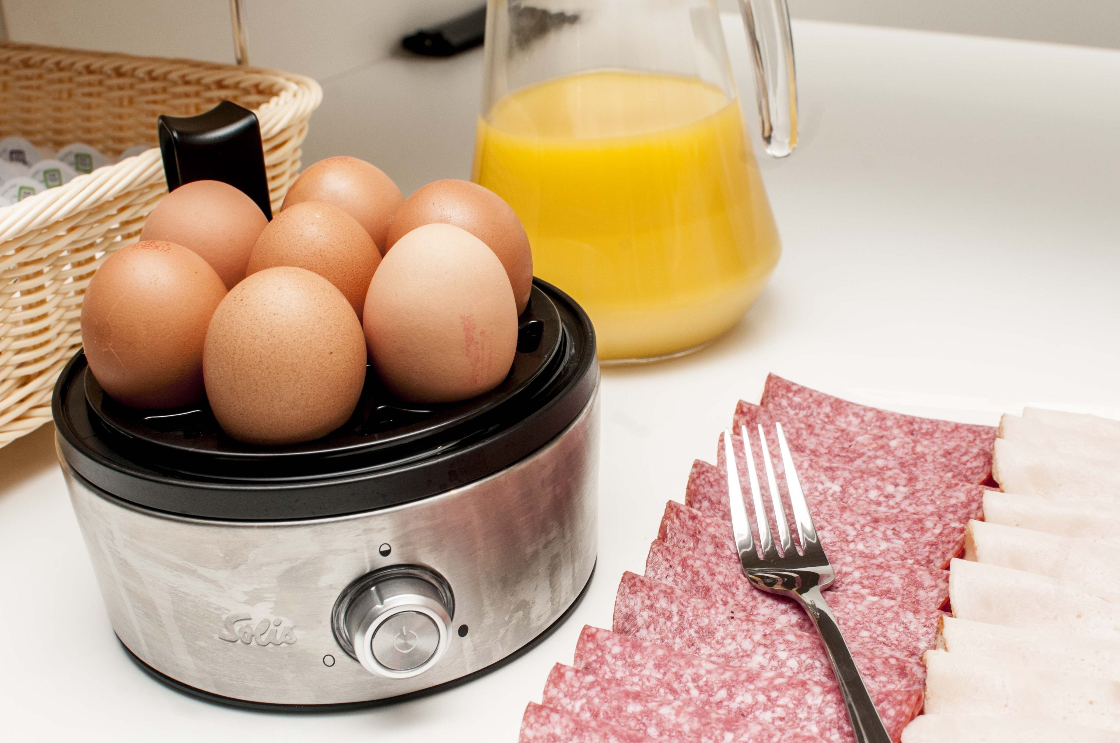 Une cuisine équipée d’un robot culinaire, avec des œufs, un verre de jus d’orange et des tranches de salami.