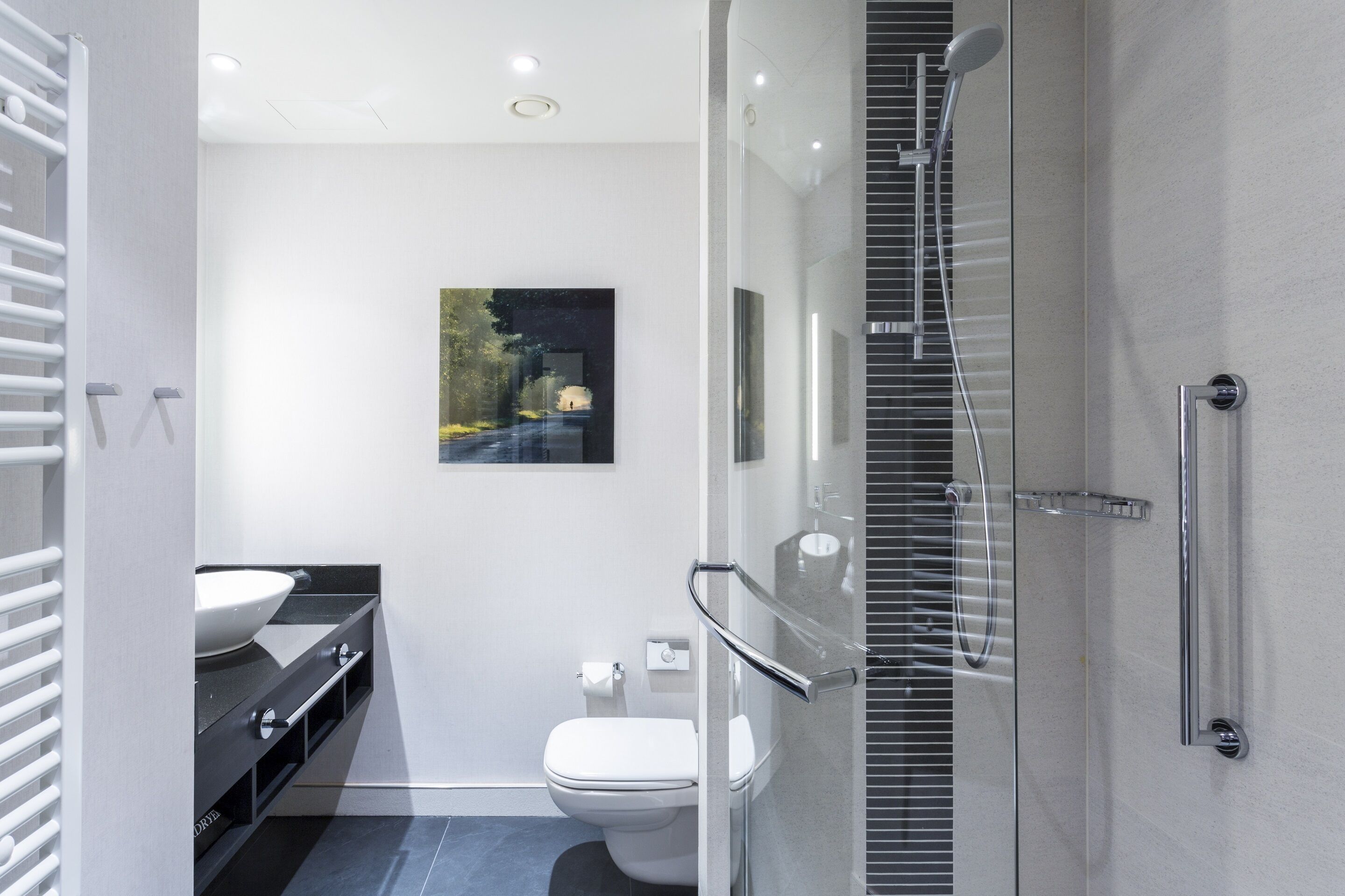 Et moderne badeværelse med brusekabine i glas, et hvidt toilet og en sort kommode med hvid vask.