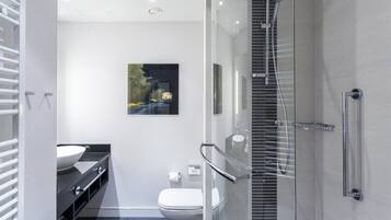 Et moderne badeværelse med brusekabine i glas, et hvidt toilet og en sort kommode med hvid vask.