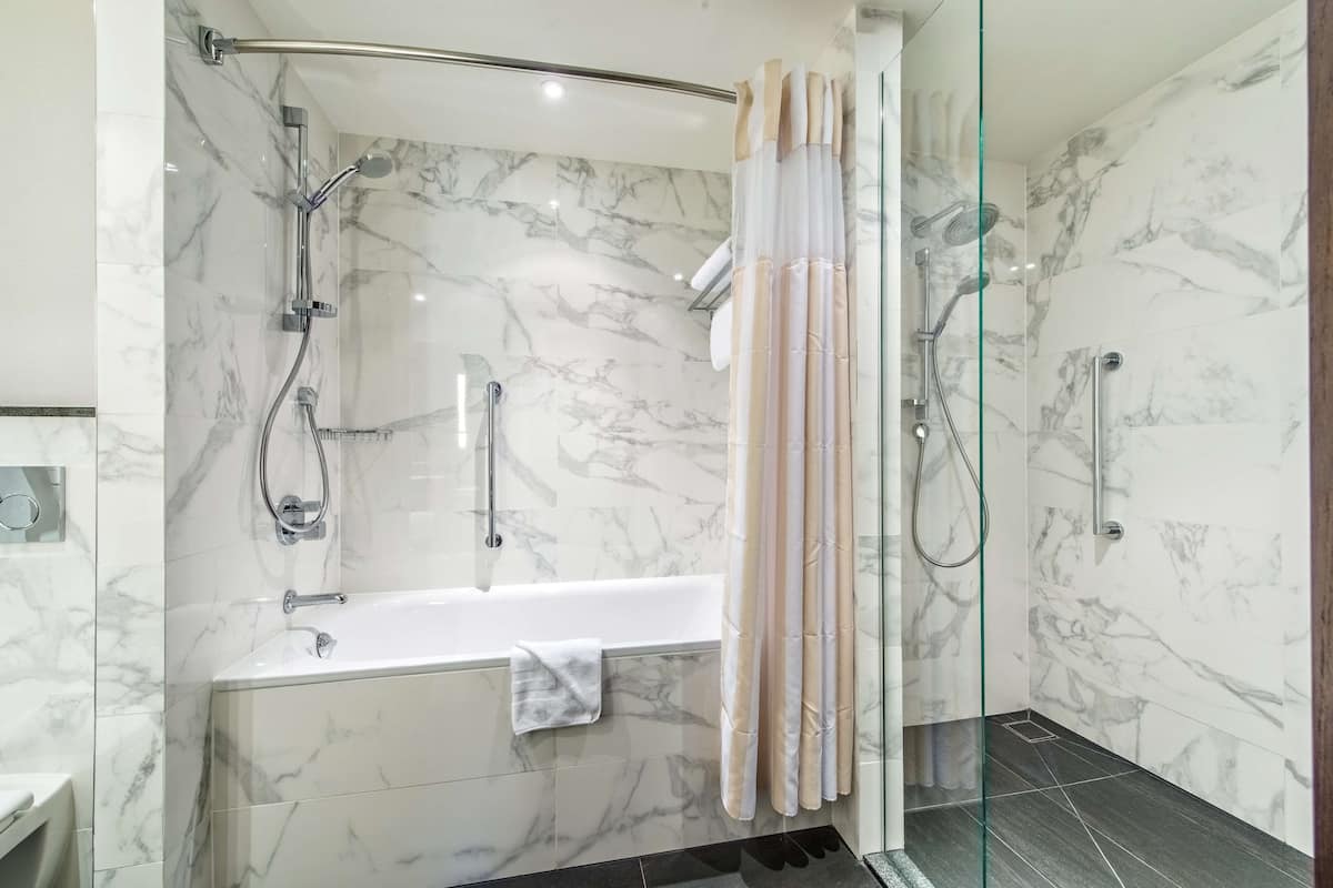 Une salle de bain moderne dotée d’une baignoire, d’une douche et d’un espace de douche séparé par des parois en verre, le tout avec des murs en marbre.