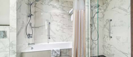 A modern bathroom with a bathtub, shower, and glass-enclosed shower area, all with marble walls.