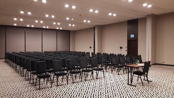 A conference room with rows of chairs, a patterned floor, and ceiling lights.