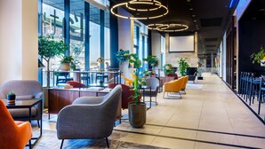 A modern hotel lobby with seating areas, large windows, and indoor plants.