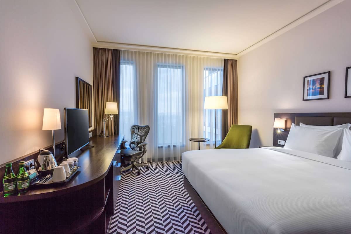 Une chambre d’hôtel avec un lit, un bureau avec une télévision, une chaise, une petite table et des rideaux.