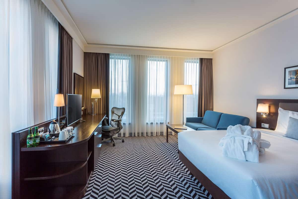 Une chambre d’hôtel équipée d’un lit, d’un bureau avec un ordinateur, d’une chaise, d’un canapé et d’une télévision.