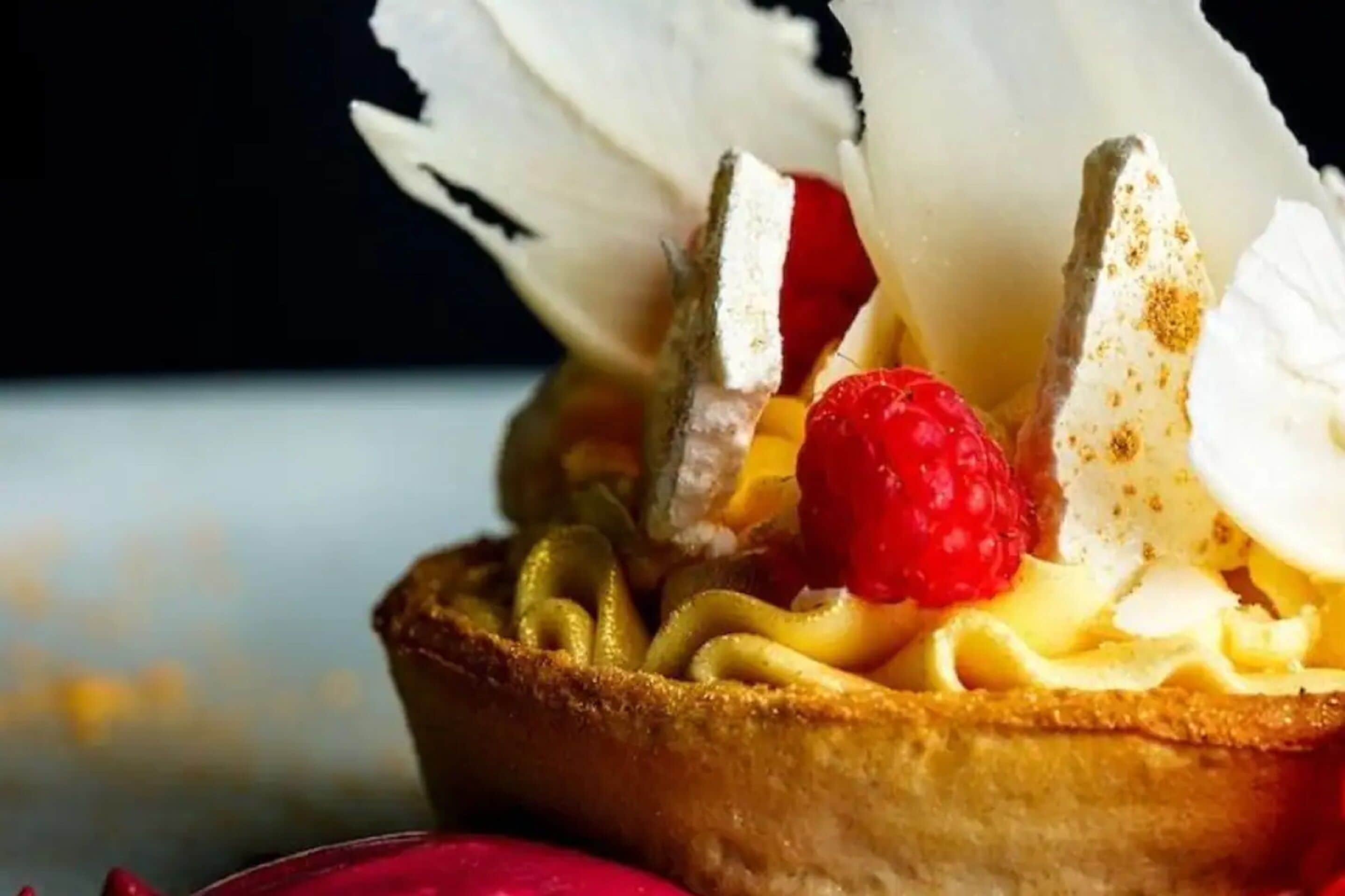 A dessert with a golden-brown crust, topped with whipped cream, a raspberry, and a decorative element.