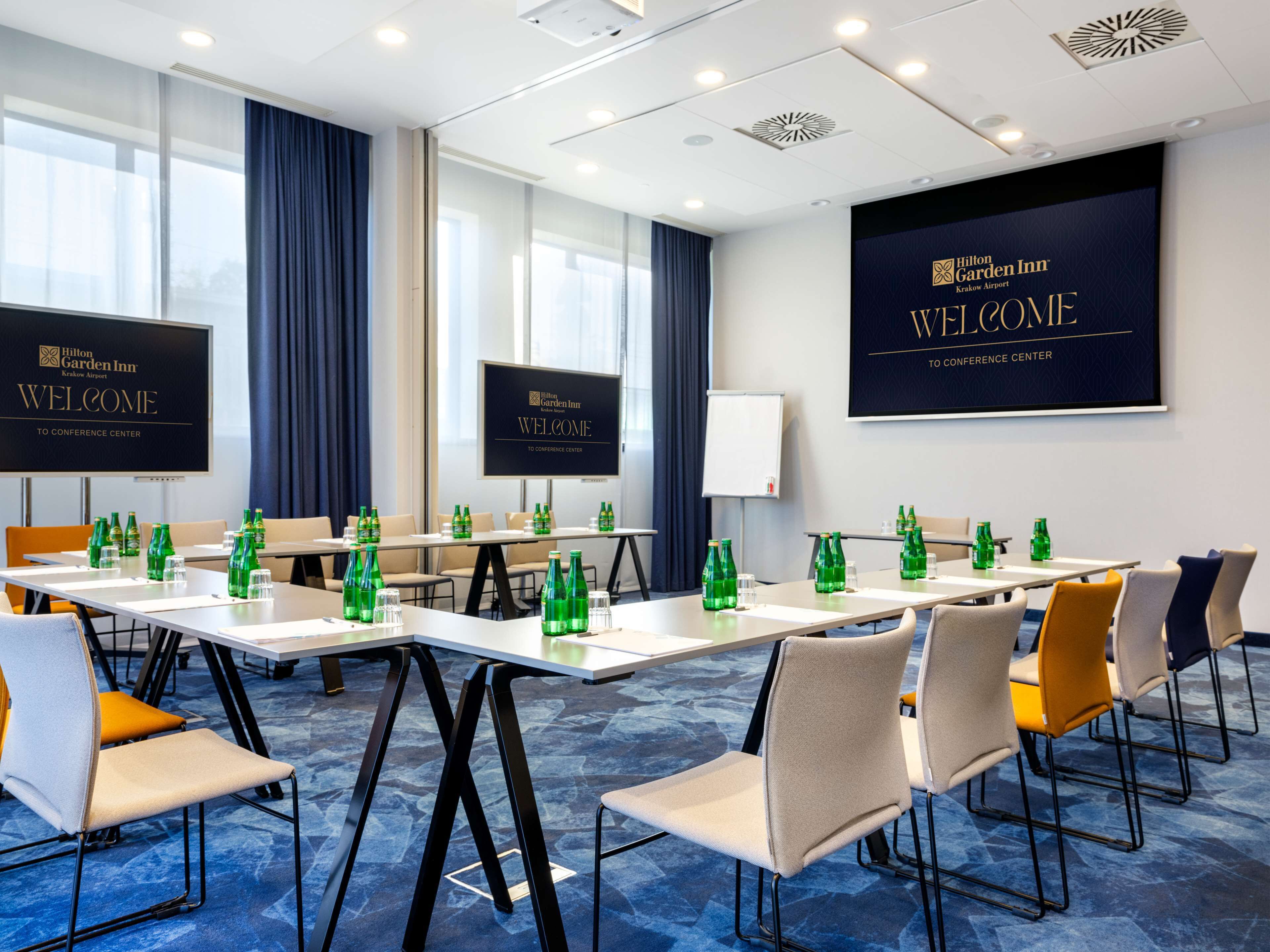 A conference room with tables, chairs, and a large screen displaying 'Welcome to Conference Center'.