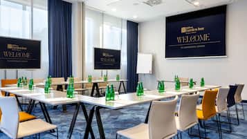 A conference room with tables, chairs, and a large screen displaying 'Welcome to Conference Center'.