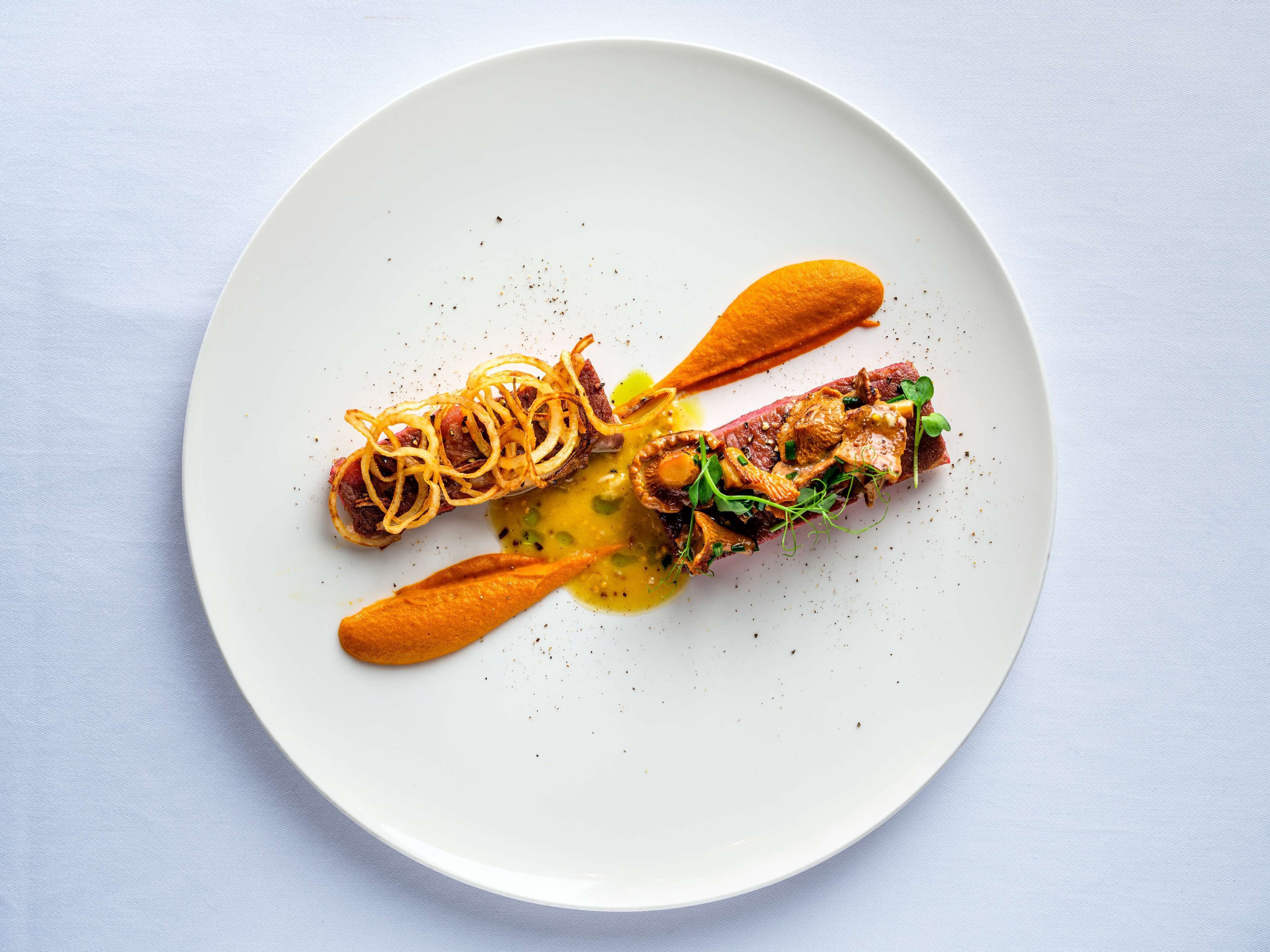 A white plate with a dish consisting of a meat fillet, vegetables, and a sauce.